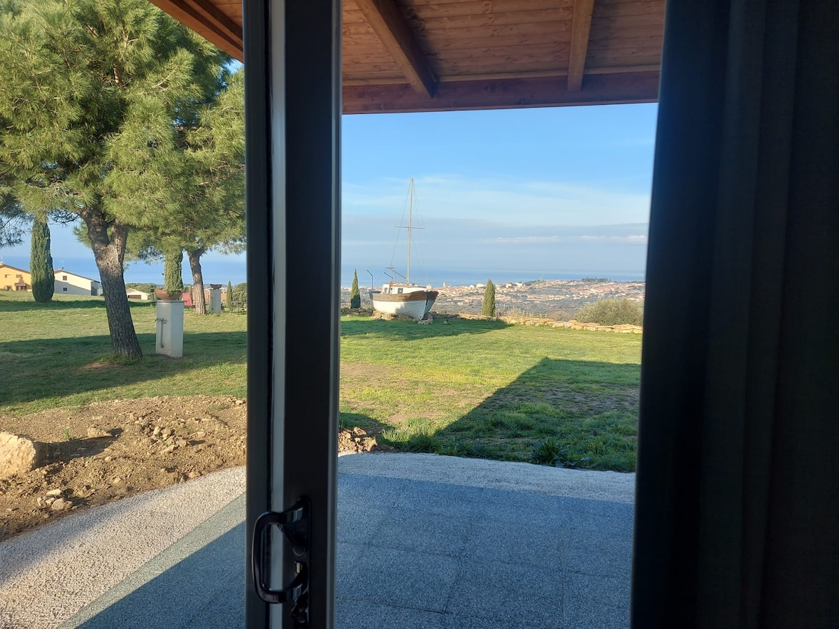 A serene outdoor view is visible through an open door, revealing a spacious lawn with a sailboat in the distance. The scene is enhanced by a clear sky and gentle landscape, featuring pine trees that flank the area.