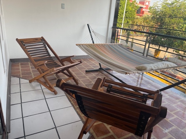 A cozy balcony is equipped with a striped hammock and two wooden reclining chairs. The tiled floor is complemented by peaceful outdoor views, providing an inviting space for relaxation.