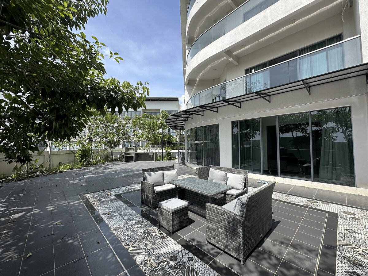A private outdoor area is showcased with lounging furniture set upon patterned tiles. Surrounding greenery provides a natural setting, while large glass doors lead into the interior space. The terrace is perfect for relaxation and social gatherings in a serene environment.