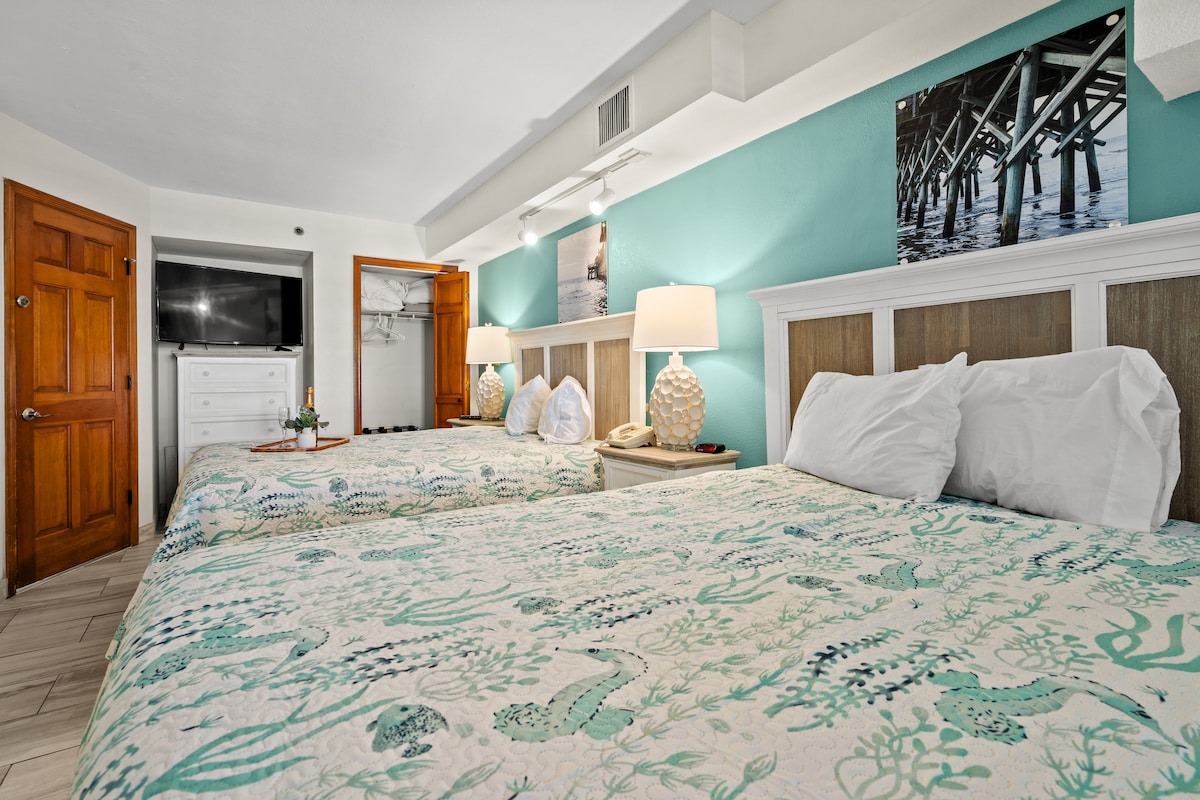 Chambre Vibrant Beach Cove avec des couleurs brillantes, deux lits queen confortables, une télévision intelligente, une commode et un placard pour plus de rangement. Un décor côtier lumineux crée une atmosphère joyeuse et relaxante pour votre escapade.