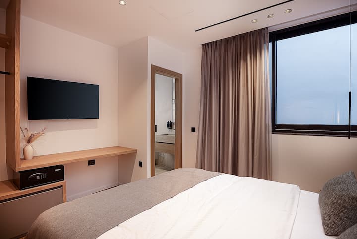 เตียงคู่ (1.70 ม. x 2.00 ม.) ห้องน้ำในตัวพร้อมที่อาบน้ำแบบยืน ตู้เสื้อผ้าแบบเปิดพร้อมตู้นิรภัย หน้าต่าง และทีวีขนาด 43”