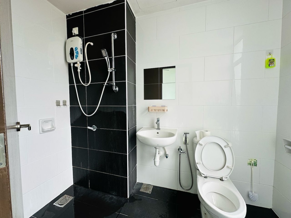 A clean bathroom features a modern shower with a handheld option, a wall-mounted mirror, and a compact sink. The toilet is positioned beside the sink, with black and white tiled walls and floor contributing to a sleek aesthetic.