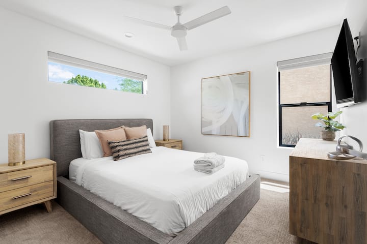 A clean, calm aesthetic meets cozy comfort in this beautifully designed room. Enjoy the soft bed, sleek fan, TV, and natural touches that make this space feel like home.