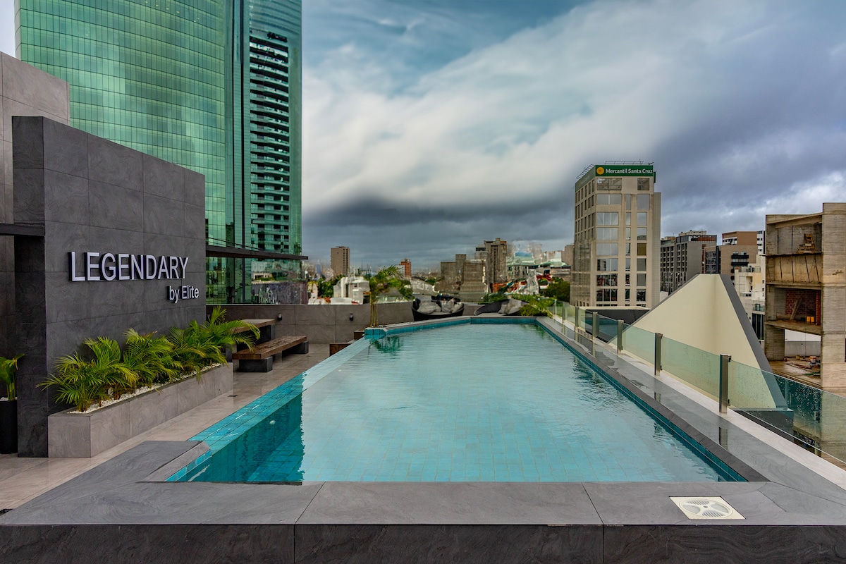 A rooftop swimming pool is featured, surrounded by sleek gray tiles and complemented by modern lounge seating. The city skyline is visible in the background under an overcast sky, creating a relaxed yet contemporary ambiance.