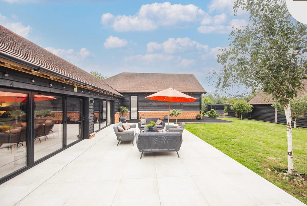 A spacious patio area is showcased, featuring comfortable seating surrounded by green grass. Two vibrant orange umbrellas provide shade, while large sliding glass doors offer a view into the house, creating a seamless transition between indoor and outdoor spaces.