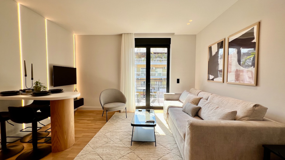 A modern living area is highlighted by a cozy sofa and a glass coffee table on a textured rug. Soft light filters through large windows covered by sheer curtains, illuminating the stylish decor and minimalistic dining space with a round table and elegant chairs.