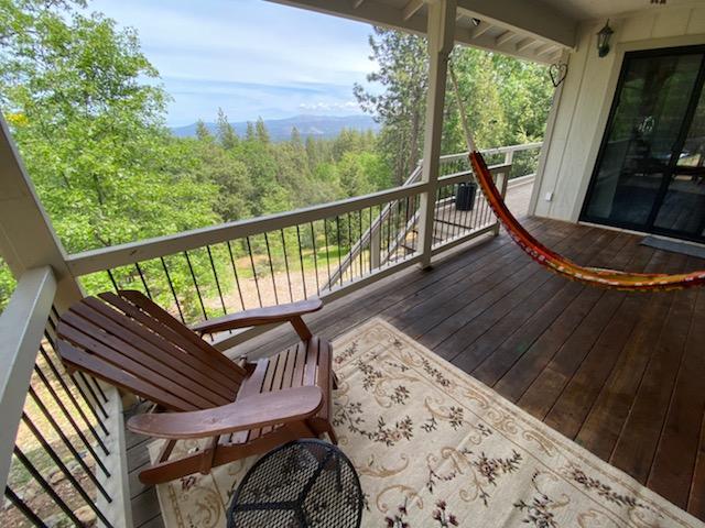 A spacious porch features a wooden hammock and an Adirondack chair positioned beside a small table. The balcony overlooks a scenic view of trees and distant mountains, with a patterned rug adding comfort to the outdoor space.
