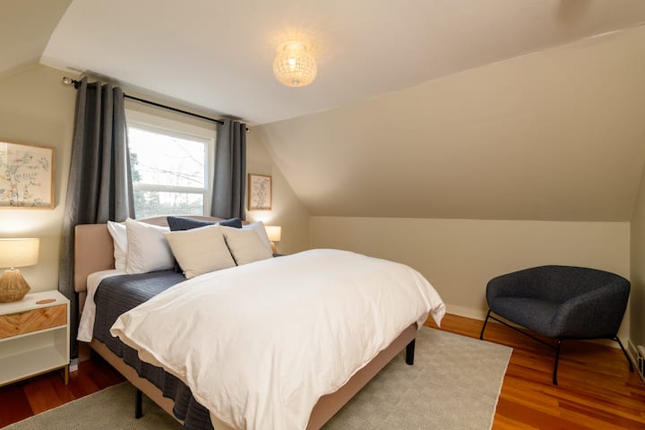 غرفة نوم في الطابق العلوي بسرير كبير وأغطية نوافذ مظلمة للغرفة وخزانة ملابس وخزانة ملابس.