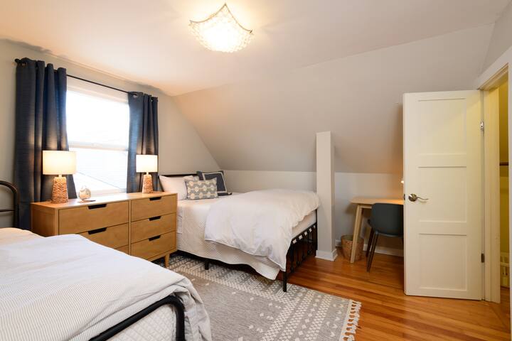 غرفة نوم في الطابق العلوي بسريرين مزدوجين وأغطية نوافذ مظلمة للغرفة وخزانة ملابس ومكتب للكتابة وخزانة ملابس.