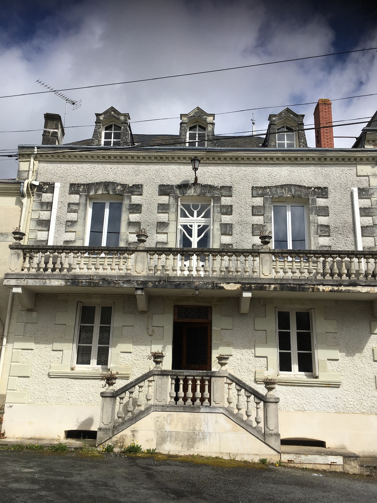 The historic residence is depicted, featuring a symmetrical façade with ornate stone details. The entrance is framed by a decorative balcony, and large windows are present on both levels. The roof is characterized by gabled sections and chimney stacks, adding to the property's charm.