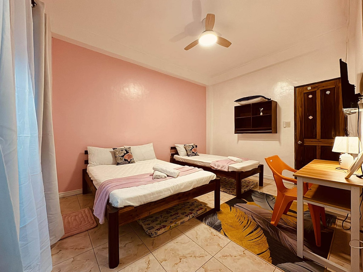 חדר שינה מקסים בצבע ורוד עדין עם שתי מיטות נפרדות עם מצעים לבנים ושמיכות בצבע ורוד. הנכס כולל טלוויזיה המורכבת על הקיר, מלתחה מובנית, שולחן כתיבה עם כיסא ומנורה, מאוורר תקרה ווילונות מהרצפה עד התקרה לפרטיות.