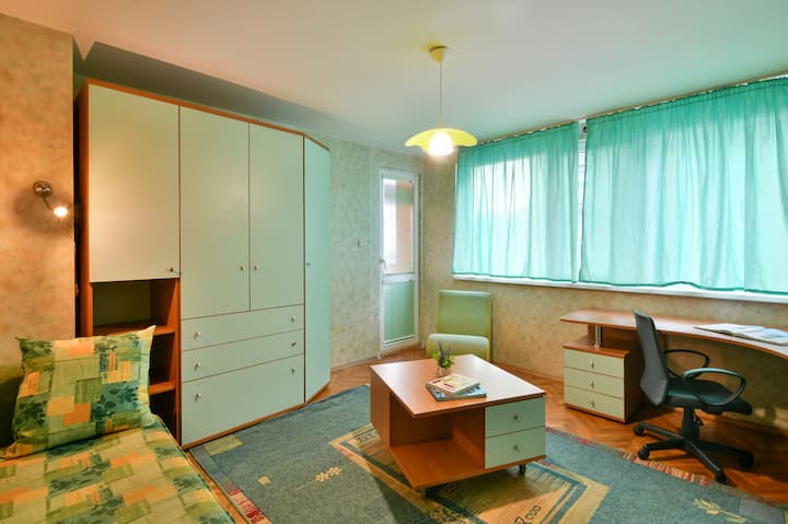 Amplio dormitorio con sofá cama y escritorio grande. Los muebles de color azul claro con detalles de madera, una alfombra azul y una mesa de centro crean un espacio acogedor y elegante para trabajar, descansar y relajarse.
