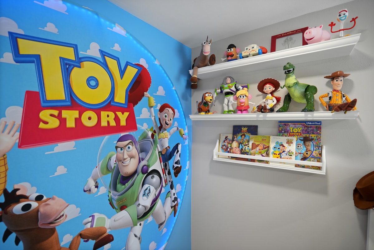 A vibrant Toy Story-themed room features a colorful wall mural with beloved characters. Shelves display a variety of plush toys and books related to the franchise, creating a playful environment for children.