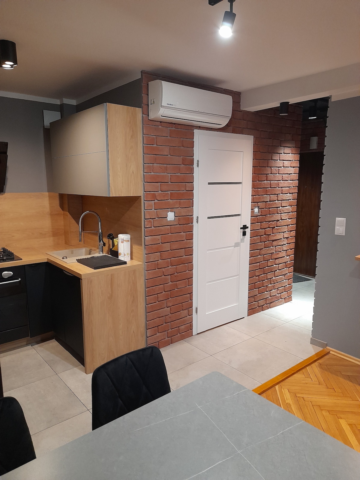 The kitchen area features modern cabinetry in a mix of wood and dark finishes, complemented by a stylish backsplash. A stainless steel sink is positioned near the entrance, which is framed by a contemporary door with a panel design. Soft lighting enhances the overall ambiance.
