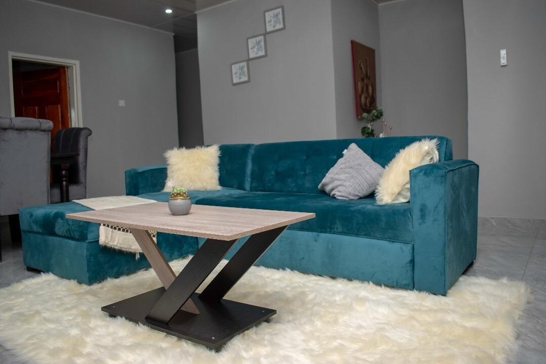 A teal sectional sofa is positioned next to a light-colored furry rug, contributing to a cozy feel. A minimalist coffee table with a wooden top and metal base sits in front of the sofa, while decorative pillows add subtle texture.