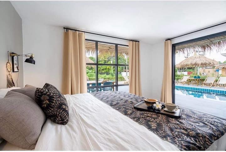 חדר שינה בקומת הקרקע עם חלונות זכוכית נפתחים שמובילים ישירות אל דק הבריכה.