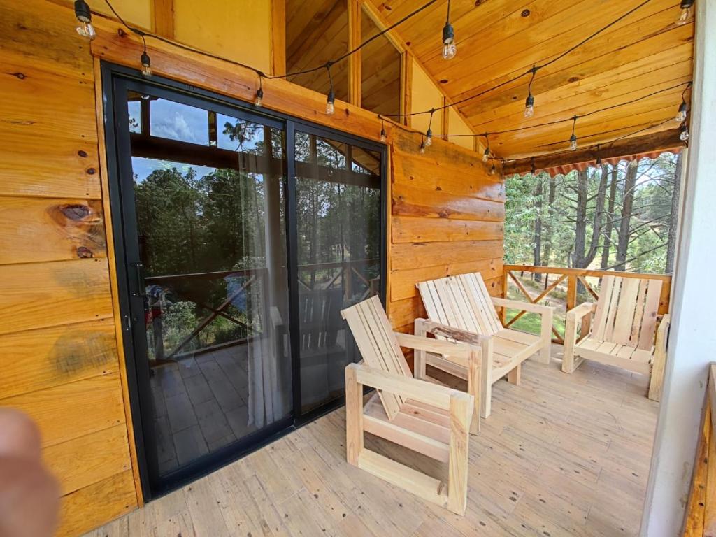 A charming elevated terrace is visible, featuring two wooden chairs and a railing that provides a view of the surrounding nature. Soft lighting is strung overhead, complementing the natural wood tones of the structure. The floor is crafted from light-colored wood, enhancing the outdoor ambiance.