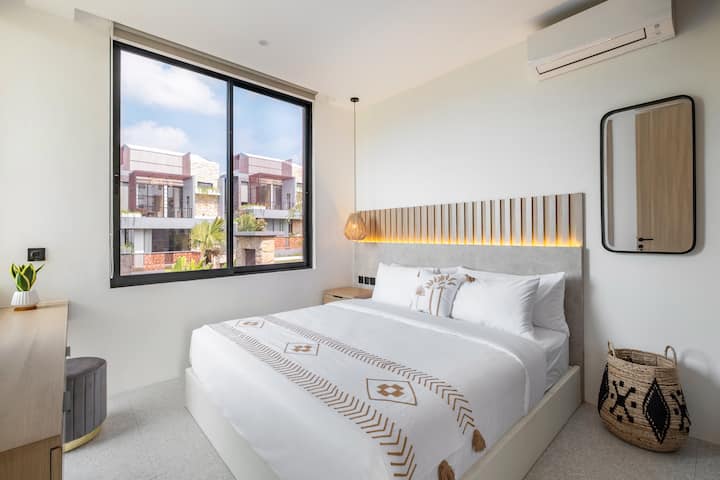 חדר שינה מואר ונעים עם נוף ירוק פנורמי וגווני עץ טבעיים.