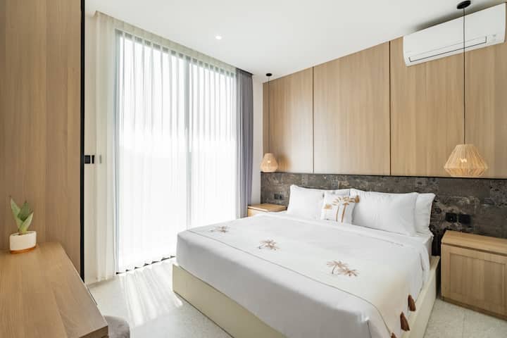 חדר שינה מואר ונעים עם נוף ירוק פנורמי וגווני עץ טבעיים.