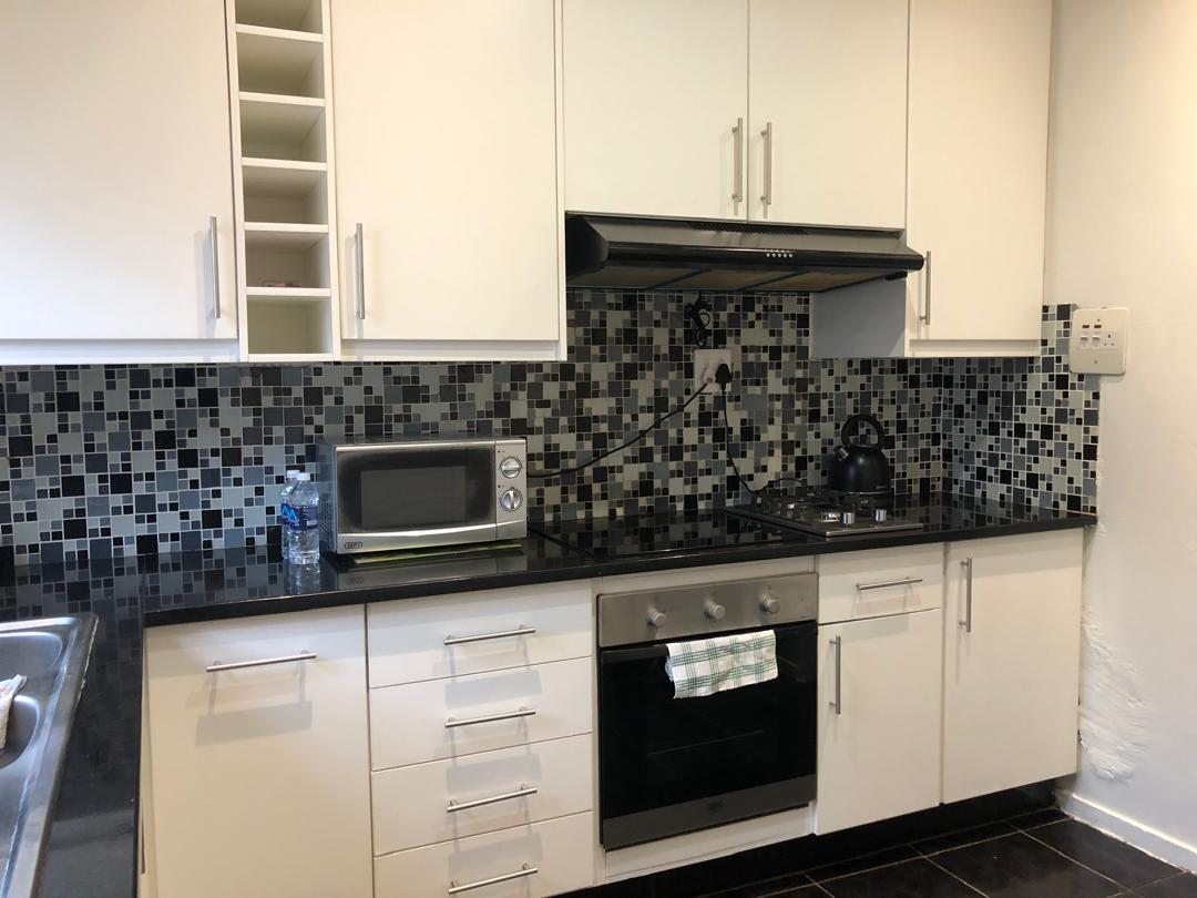 A well-equipped kitchen features sleek white cabinetry contrasted by a patterned black and white backsplash. Stainless steel appliances, including an oven and microwave, are arranged thoughtfully. A kettle sits on the stovetop, and a bottle of water is visible on the countertop.