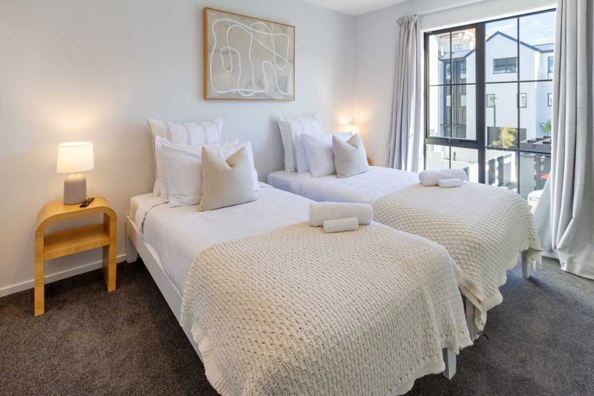 Esta habitación cuenta con dos camas individuales, cada una con cómodos colchones y sábanas frescas. Las ventanas de vidrio altas ayudan a traer luz natural a la habitación, por lo que es más hogareña