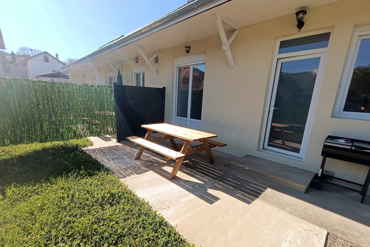 A private terrace area is seen, featuring a wooden picnic table surrounded by greenery. The concrete surface provides a comfortable setting, while a decorative screen offers additional privacy. Natural light brightens the space, enhancing the outdoor experience.