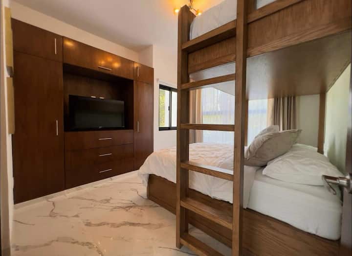 Chambre au premier étage avec lit king size, lit superposé et lit simple. Elle dispose d'une télévision connectée avec accès à des plateformes de divertissement et d'une salle de bain privée, idéale pour les familles ou les groupes.
