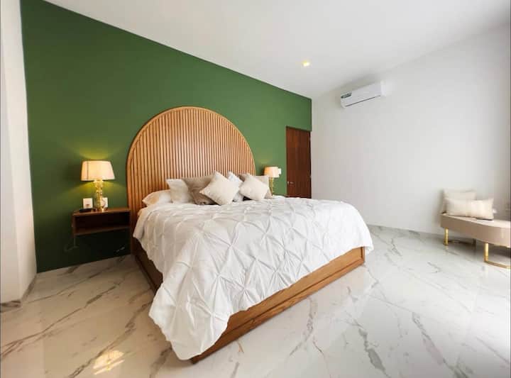 Chambre principale au premier étage avec lit king size et vue sur la jungle. Elle dispose d'une télévision connectée avec accès à des plateformes de divertissement, d'un dressing ouvert pour placer les valises et les vêtements, et d'une salle de bain privée complète.
