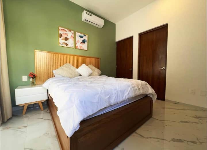 Chambre principale au rez-de-chaussée avec lit queen size et vue sur la jungle. Elle dispose d'une télévision connectée avec accès à des plateformes de divertissement, d'un dressing ouvert pour placer les valises et les vêtements, et d'une salle de bain privée complète.
