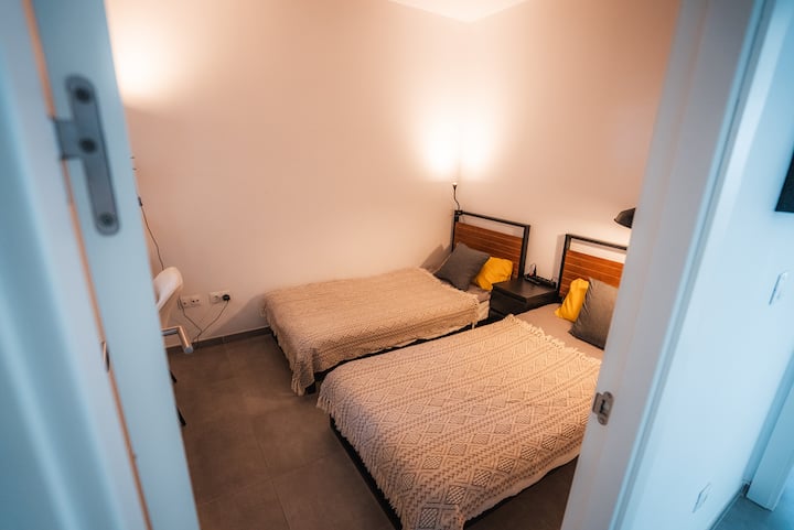 ห้องนอนพร้อมเตียงเดี่ยว 2 เตียงเหมาะสำหรับเพื่อนหรือเด็กตกแต่งด้วยสิ่งทอที่เป็นกลางและแสงไฟอุ่นๆ