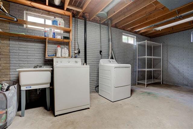 A functional laundry area is visible, featuring a double basin laundry sink alongside a front-loading washing machine and dryer. Natural light enters through small windows, illuminating the gray-brick walls. An open metal shelving unit is positioned in the corner, offering additional storage options.
