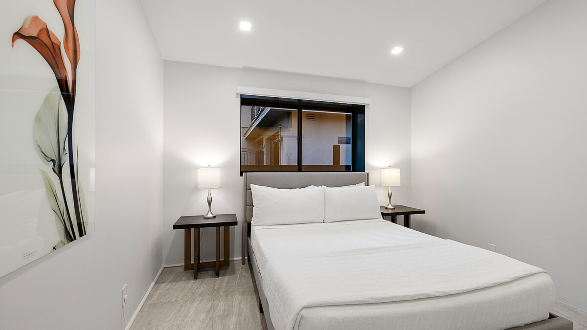 მზით განათებული, ჰაეროვანი საძინებელი 2, რომელშიც არის კომფორტული 152×203 სმ ზომის საწოლი, ხელოვნების ნამუშევრები და ბუნებრივი სინათლე.