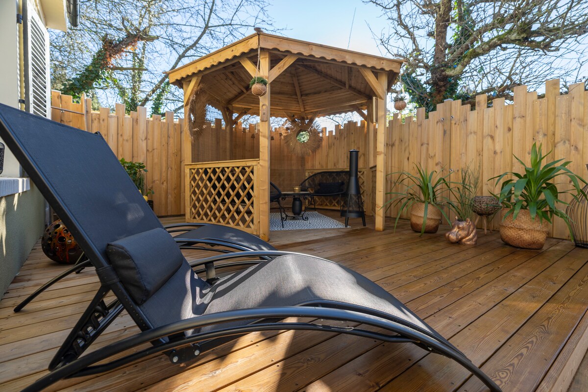 A private terrace features wooden decking with lounge chairs positioned for relaxation. In the center, a gazebo provides a shaded area, surrounded by decorative plants and a wooden fence, creating a secluded space for outdoor enjoyment.