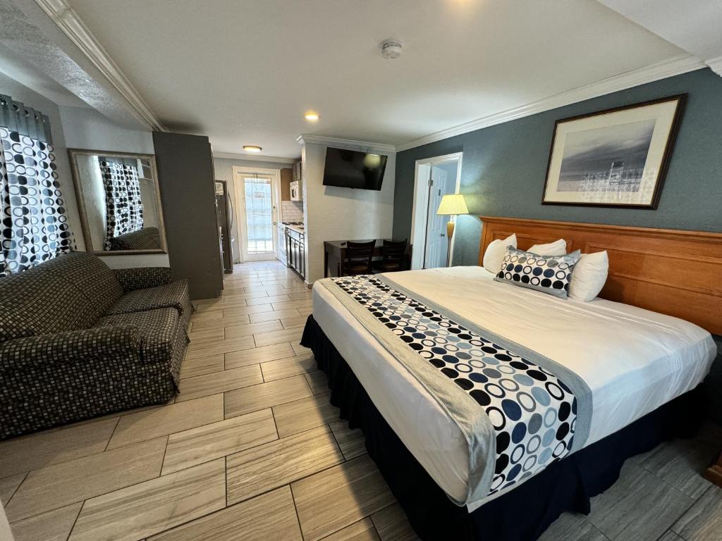 A modern suite interior features a spacious bed with patterned bedding, complemented by a cozy seating area with a patterned couch. An entertainment unit with a flat-screen TV is mounted on the wall. Natural light enters through a nearby window, illuminating the tiled floor.