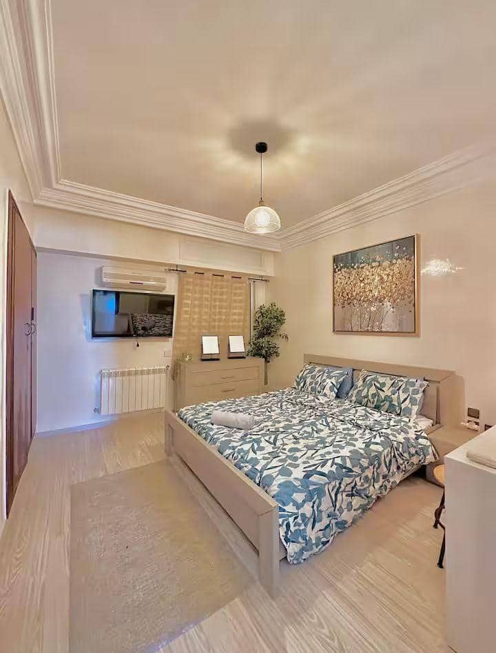 卧室配有舒适的双人床、舒适的床上用品和设计师木质床头板。壁挂电视、空调和套内卫生间，还有宽敞的存储空间和白色毛巾 