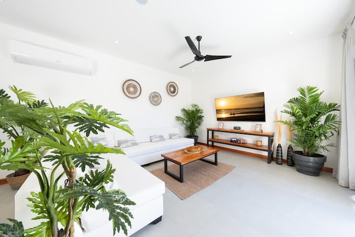 This tropical style living room is a bright and inviting space, filled with natural light and lush.  A large, comfortable sofa anchors the room.
Sliding glass doors open directly to a sparkling pool, creating a seamless indoor-outdoor connection. 
