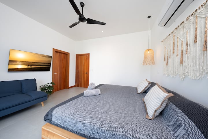 The design embraces simplicity and natural elements, with crisp white walls, light wood furnishings, and subtle touches of greenery that highlight the coastal ambiance.