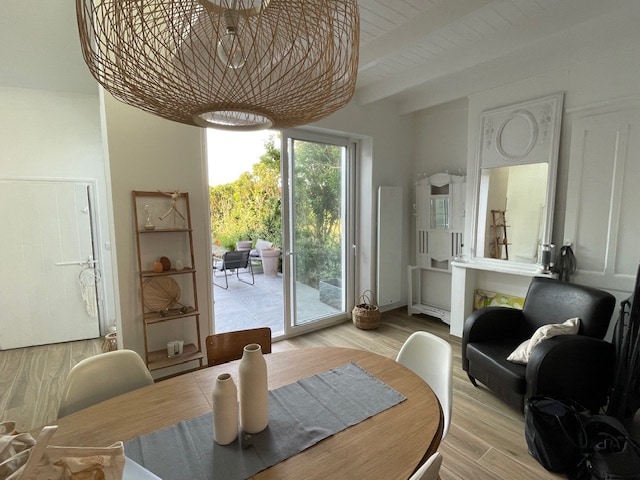 A well-lit dining area features a round wooden table set with three white vases. A woven light fixture hangs above, adding a unique element. Adjacent, floor-to-ceiling glass doors open to the outdoor terrace, showcasing a glimpse of greenery and patio seating.