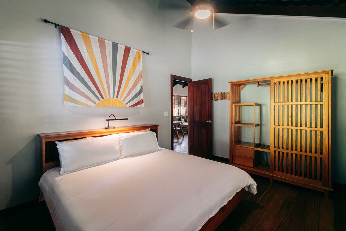 Un grand lit king size avec des draps blancs, une couette confortable, un placard personnalisé et de hauts plafonds rendent cette chambre confortable mais aérée