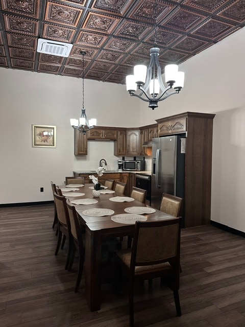 A modern kitchen area showcases dark wood cabinetry and stainless steel appliances. A long dining table with eight chairs is prominently featured, set for a meal with decorative placemats. A statement chandelier hangs from the ceiling, complementing the intricate design above.