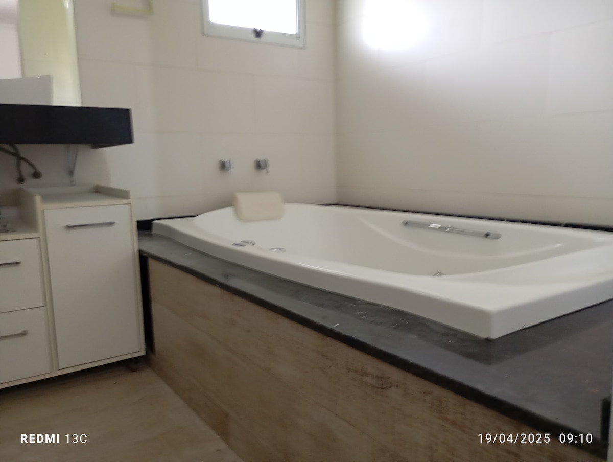 The bathroom features a spacious whirlpool bathtub set against a minimalist backdrop. A dark counter contrasts with light walls, while a small window allows natural light to enter the space. Storage cabinets are positioned nearby, providing additional convenience.