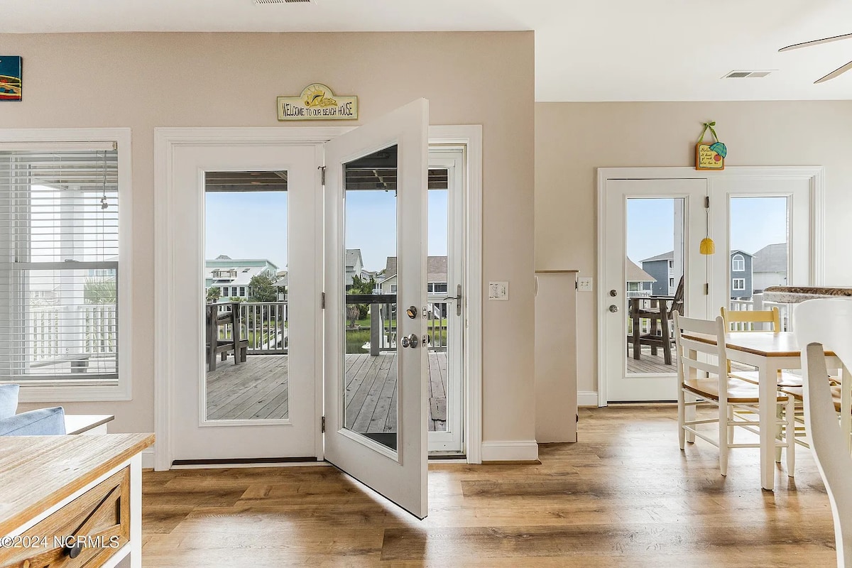 Double French doors open to a spacious deck, allowing natural light to fill the inviting living space. Light-colored walls and wood flooring create a bright atmosphere. Two pairs of glass doors lead to the outdoor area, enhancing the connection to the surroundings.