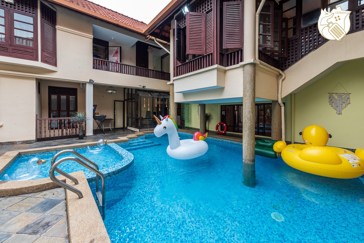 A vibrant swimming pool area is featured, showcasing a light blue pool with inflatable toys, including a unicorn and yellow duck. Surrounding the pool are polished stone surfaces, and the structure contains a mix of traditional and modern architectural elements.