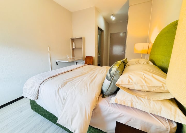 A warm and welcoming master bedroom with soft linens and a peaceful reading/study or dressing table nook to unwind or catch up on work. Make up mirror in cupboard. The en-suite bathroom adds a touch of privacy and comfort—your own space