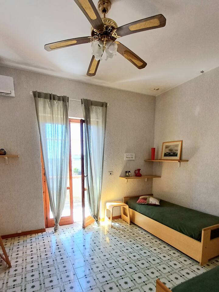 Camera da letto con 2 letti singoli, armadio, scrivania, aria condizionata, ventilatore a soffitto, balcone panoramico.