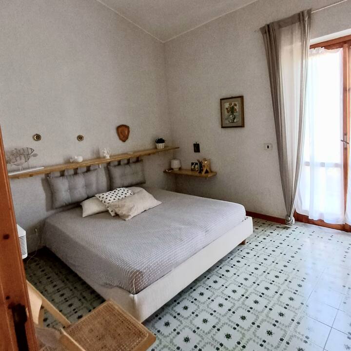 Camera da letto matrimoniale con armadio, comò e codini, aria condizionata e ventilatore a soffitto. La camera è provvista di balcone.