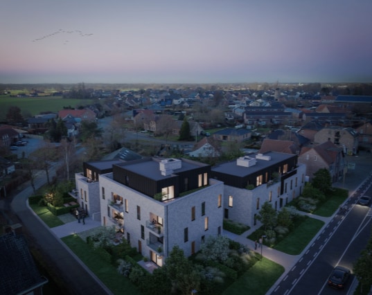 An aerial view captures a modern residential building under twilight, surrounded by green landscapes and suburban homes. Soft lighting highlights the building's contemporary architecture and landscaped areas, while the horizon displays a gentle gradient of fading daylight, suggesting a peaceful evening atmosphere.
