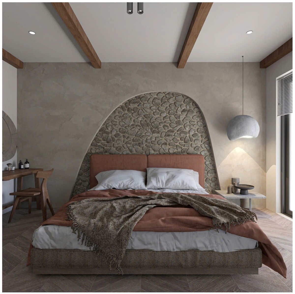 A spacious bedroom features a textured stone wall backdrop with an arched design. A large bed with neutral linens is complemented by a cozy throw at the foot. Natural light filters through a nearby window, illuminating a small bedside table and wooden chairs in the room.