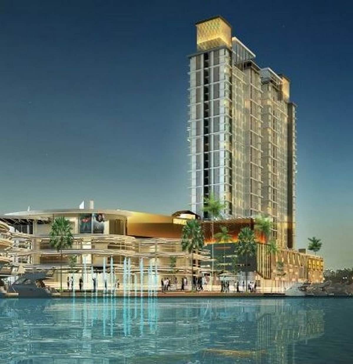 A modern high-rise building is shown next to a body of water, featuring a mix of glass and concrete architecture. The structure is illuminated, highlighting its elegant design. Surrounding palm trees add greenery to the urban setting, creating a serene atmosphere at dusk.