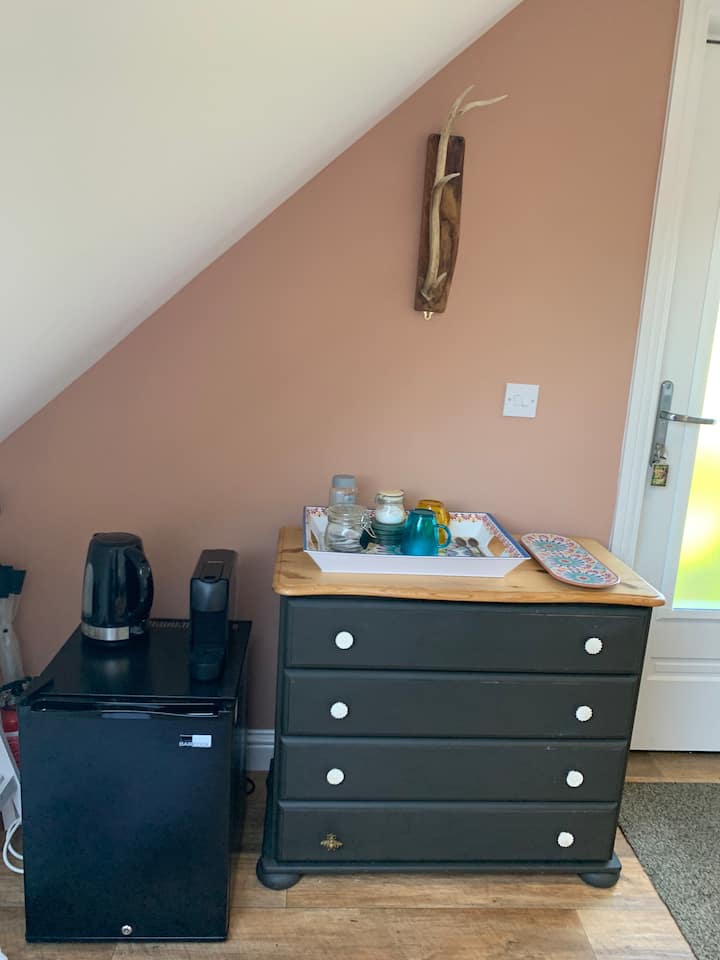 Komoda, malá tichá chladnička, rýchlovarná kanvica, Nespresso, šálky, čaj, cukor a káva. 